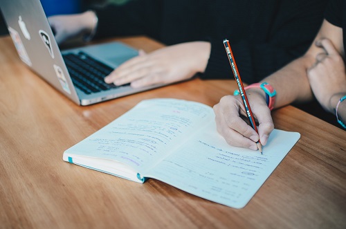 person holding a pencil looking over a notebook with writing in it