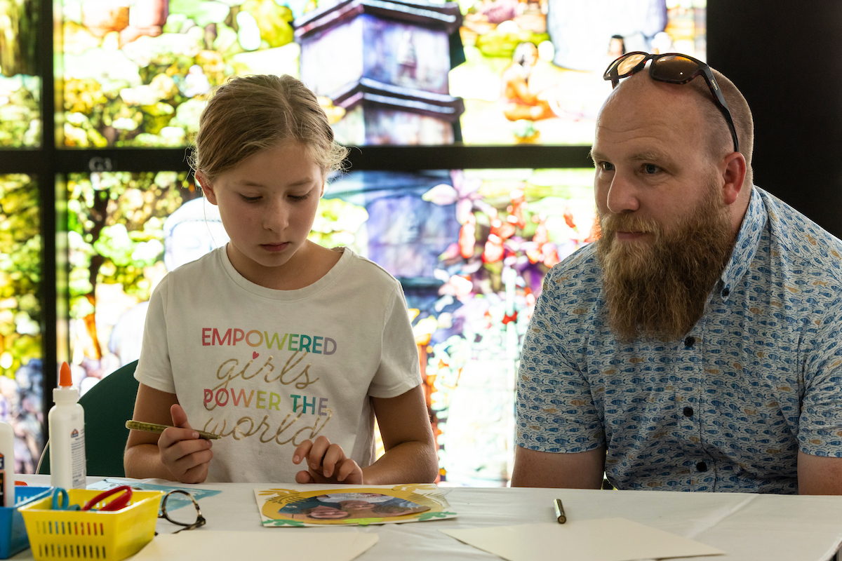 Image of child and a parent in the Roots of Knowledge, the child has painting supplies in front of them