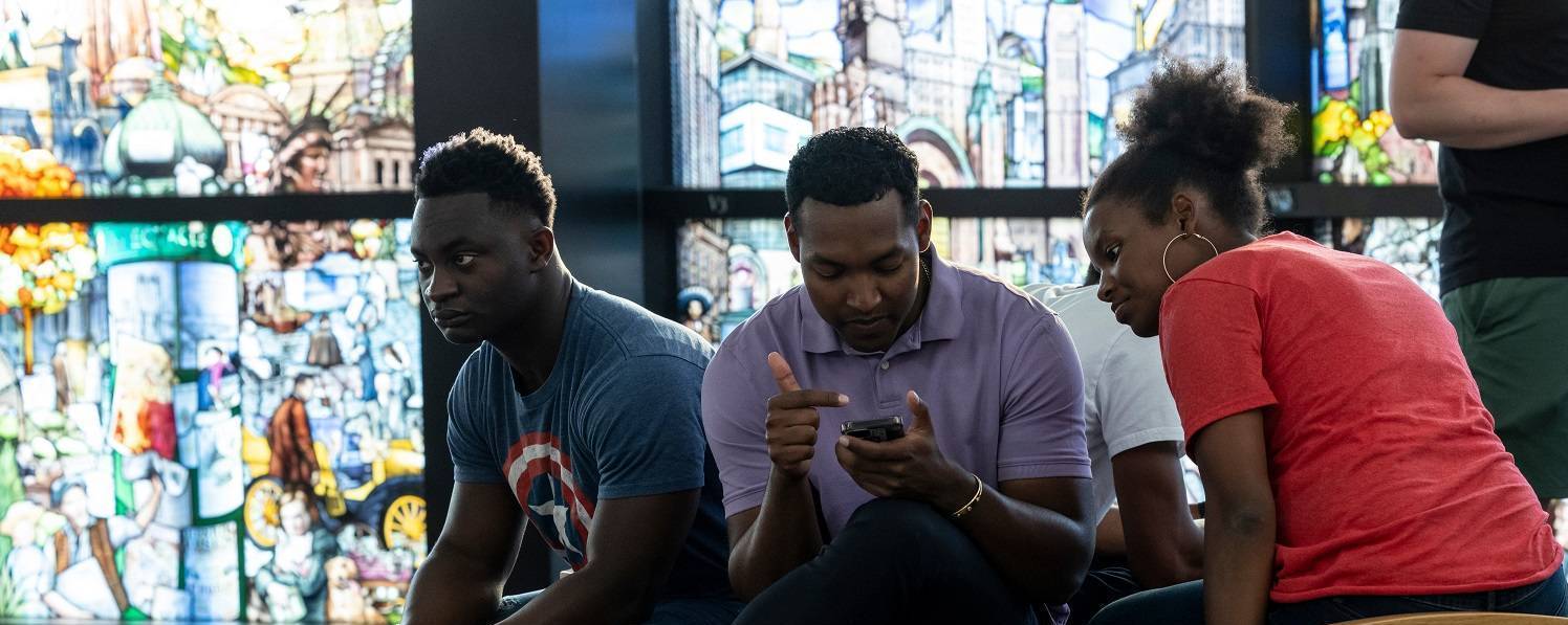 Image of students looking at a phone while seated on a bench inside the Roots of Knowledge