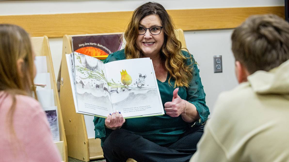 Woman reading picture book to students.