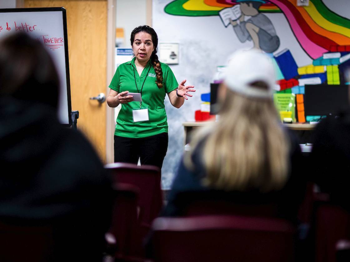 An intern in a green shirt speaks to a group of adults