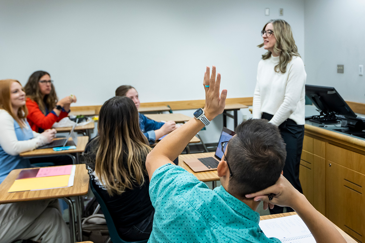 Image of a lecture with a student raising their hand.