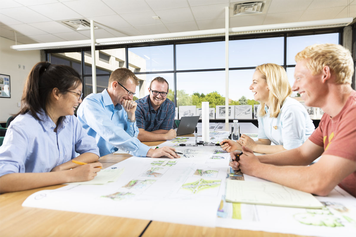 Four people talking over a table with design papers across the table.