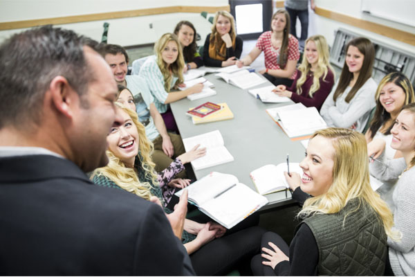 Group of students around a table talking to a teacher.