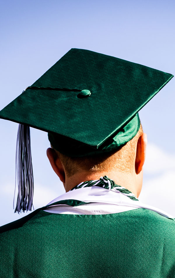 A graduating student wearing a green cap and gown.