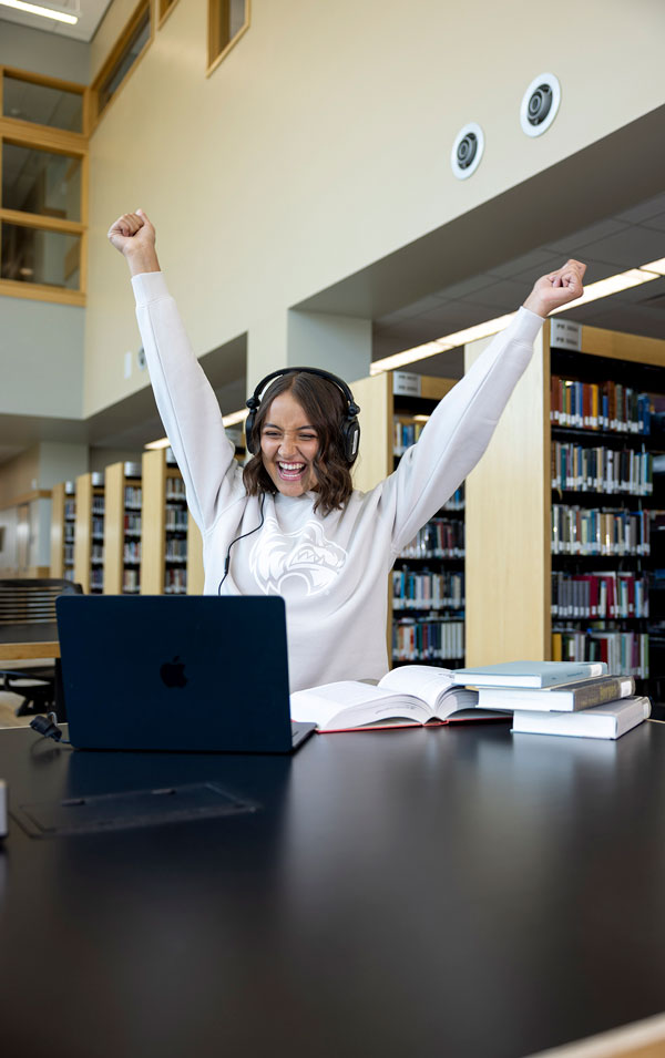 A smiling student with her arms raised in the Fulton Library.