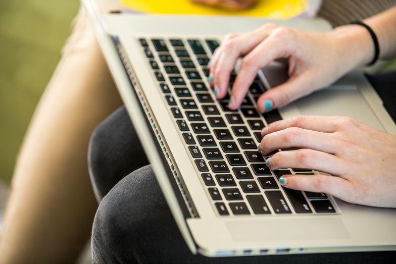 A closeup on a laptop with someone typing on the laptop.