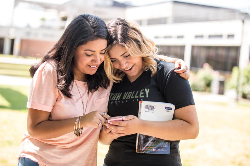 Two women standing next to each other looking at a cellphone