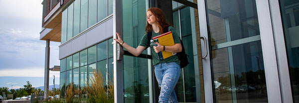 A student opening a door and carrying a stack of textbooks.