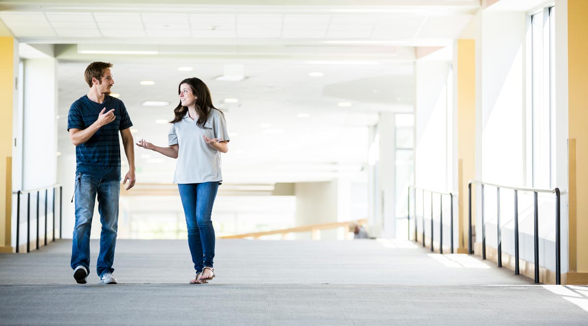 A man and a woman walking down a hallway talking to each other.