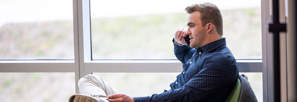 A student on the phone seated in front of a window.