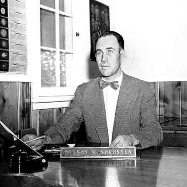 A young Wilson Sorensen sitting at the desk in his office. Black and white photo.