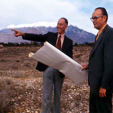 Wilson Sorensen standing outside with another man, who is holding building plans. Wilson is pointing to a spot.