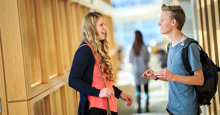 Two students standing in a hallway talking to each other.