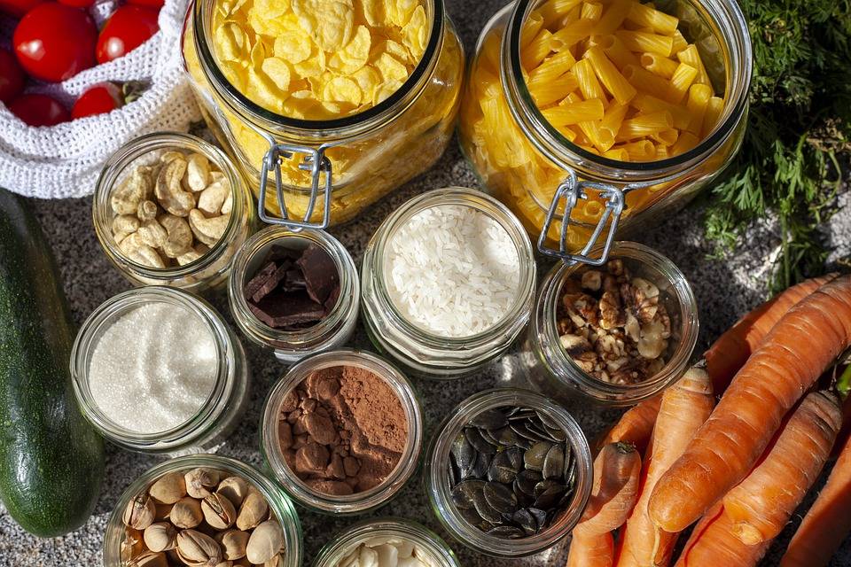 fresh vegetables surround glass jars filled with dry goods