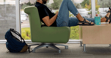 Student studying sitting in a chair, widows in the background showing part of the exterior of Orem campus.