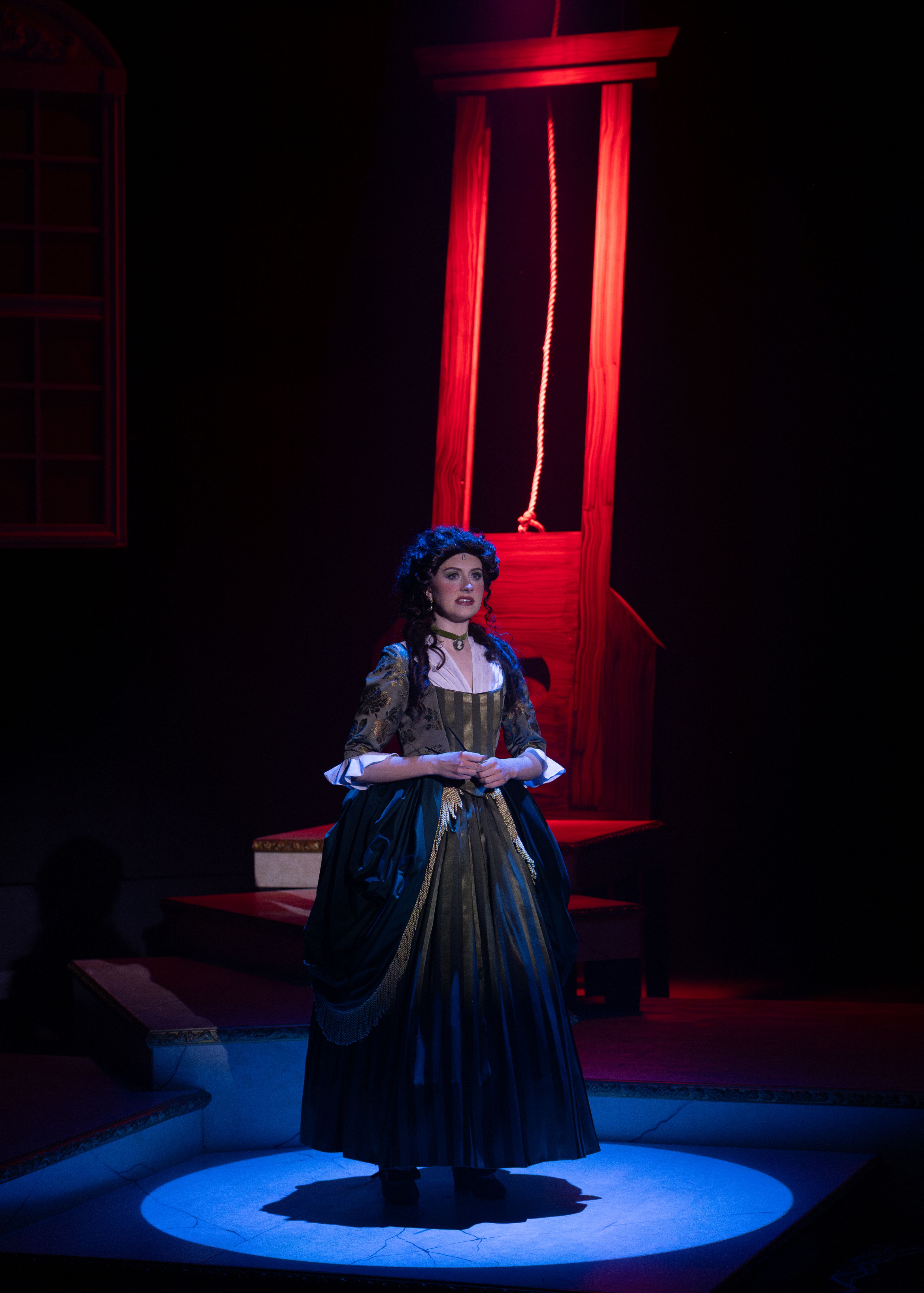Gin Mummy Theatre Performance A woman in French Revolution Era clothing, standing in a spotlight in front of a guillotine