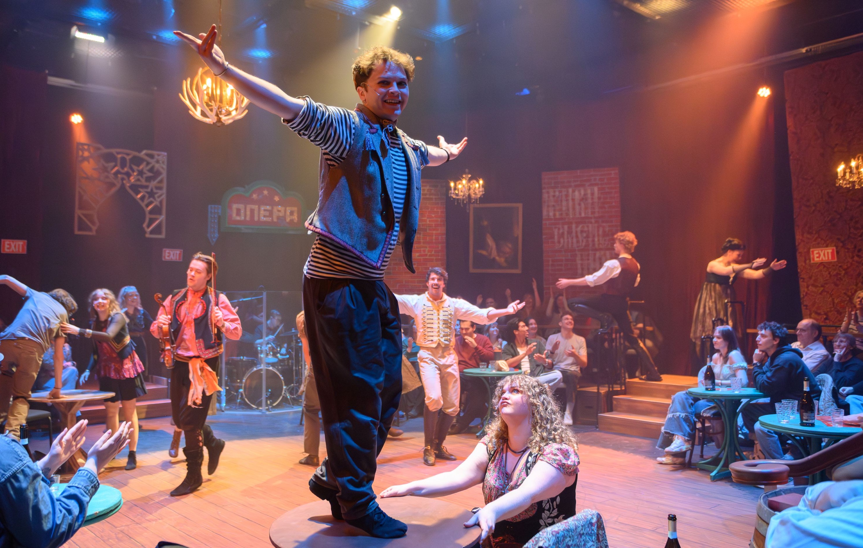 Actors dancing wilding on tables and amid the audience in a smoky arena stage