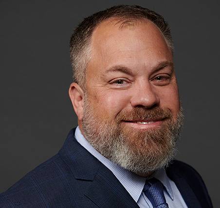 Photo of Ryan Mackerell  a caucasian male with a beard wearing a blue suit coat and tie