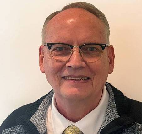 Photo of Scott Seals. He is wearing a yellow tie with a grey sweater and white shirt