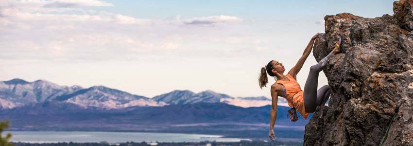 A woman free climbing up a mountain with a city off in the distance in the backdrop.