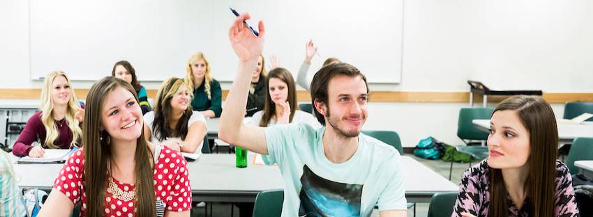 Students in a classroom with two students raising their hands to ask a question.