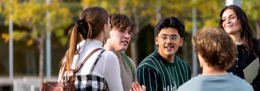 A group of students standing outside talking with one another.