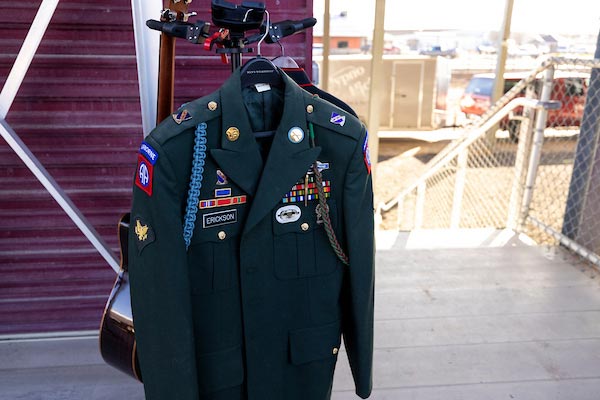 A military uniform on a hanger, with a guitar behind it.