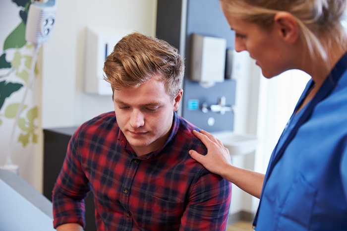 A female health professional rests her hand on a male patients shoulder