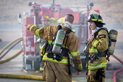 Two firefighters in full equipement, discussing how to battle a fire.