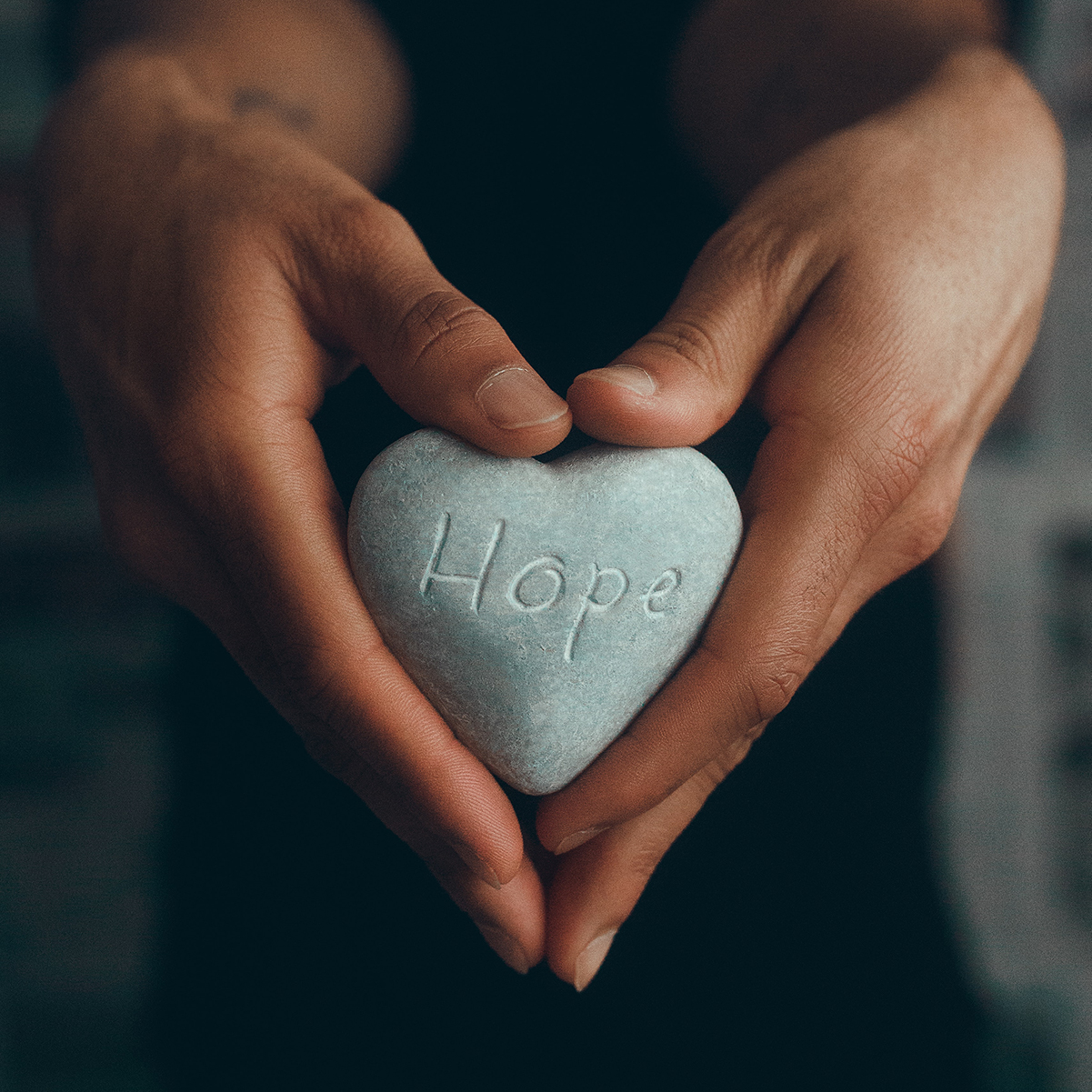 hands holding a heart-shaped rock with the word hope