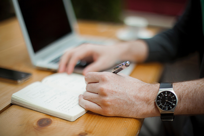 Hands writing in a notebook on a desk