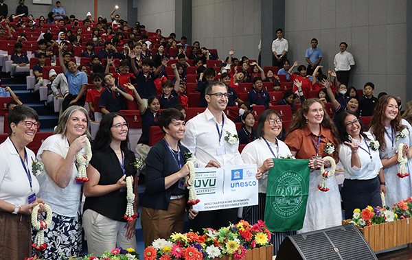 Teachers standing for a group photo in front of an audience of elementary students, holding a UNESCO banner