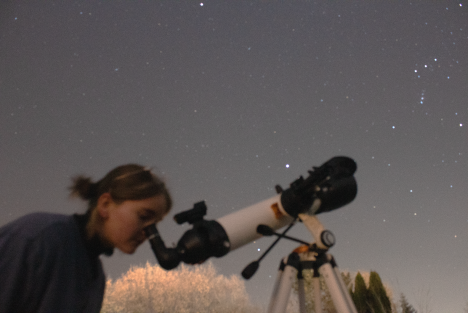 Photo of Brin Bettis looking through a telescope under a starry night sky