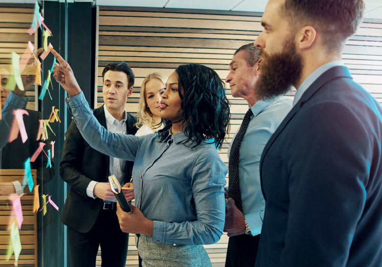 People standing in front of a glass wall with post it notes on it