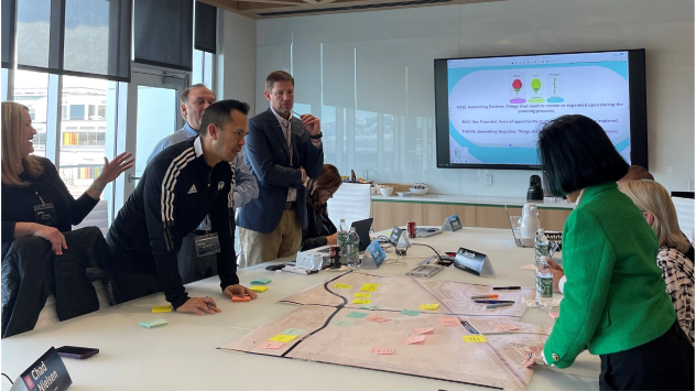 President Tuminez collaborating around a conference table with a large map, presentation screen in the background.