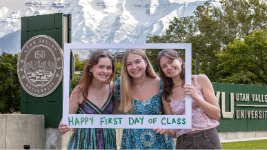 Three female students hold up a square cut out that looks like a polaroid with "Happy First Day of Class" written on it