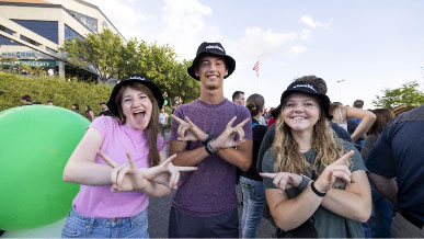 Three students standing next to each other holding up the UVU wolverine hand sign