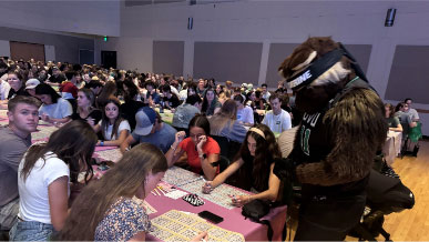 Willy the Wolverine standing next to a table of students playing bingo