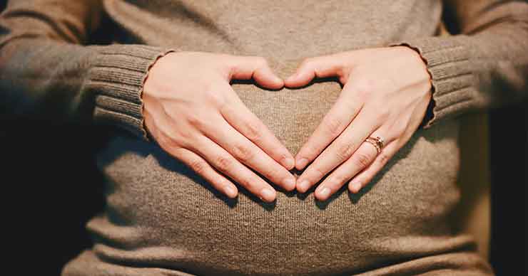 A pregnant woman with her hands on her stomach, her hand are shaped like a heart.