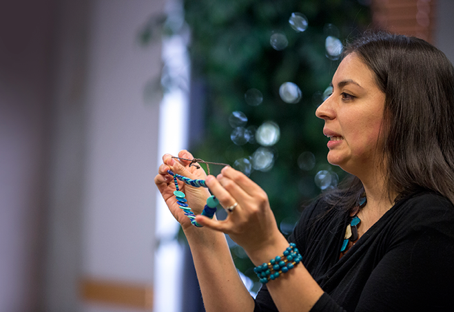 Image of woman holding up jewelrey and speaking to an audience