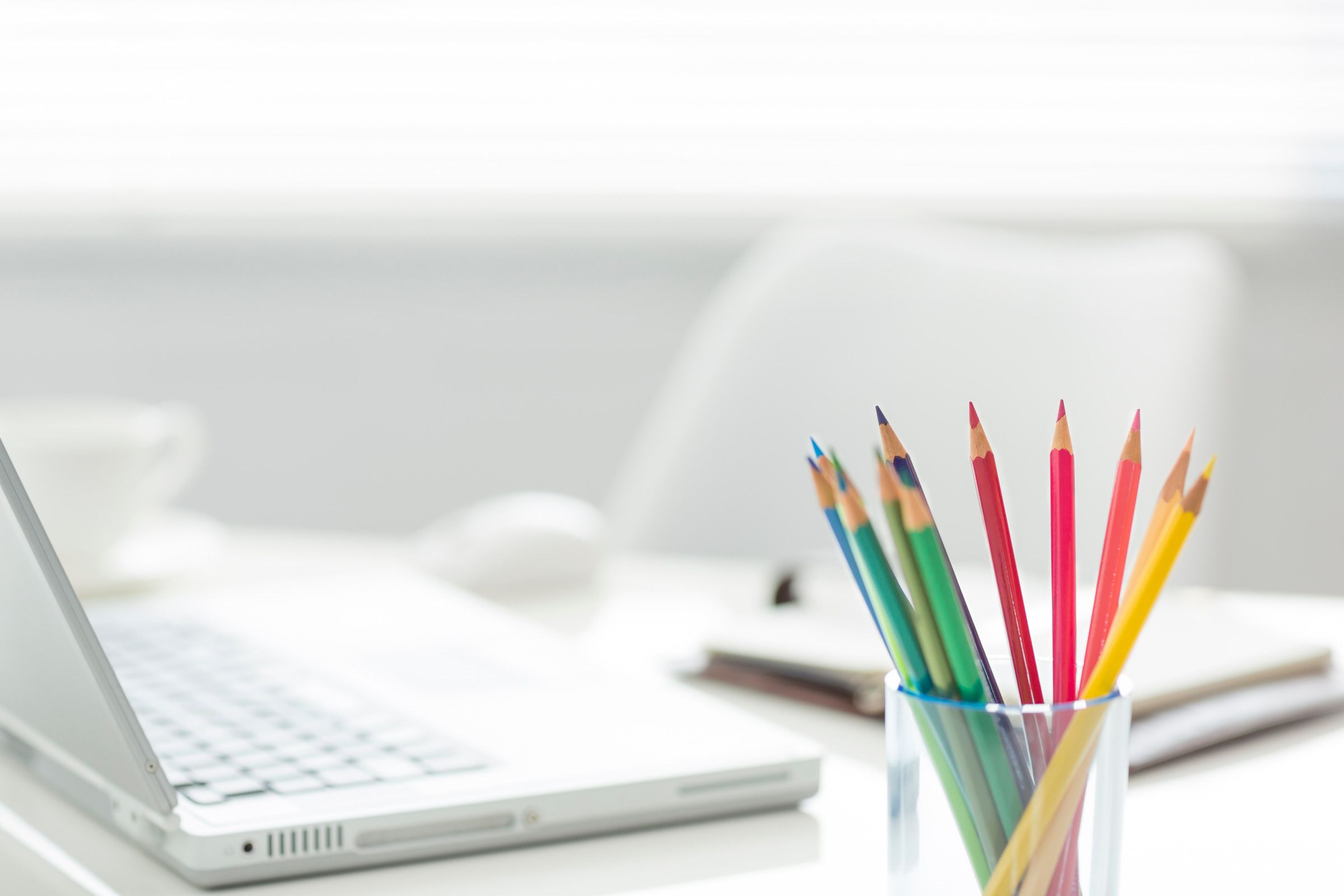 White desk with a laptop and cup of colored pencils sitting on it