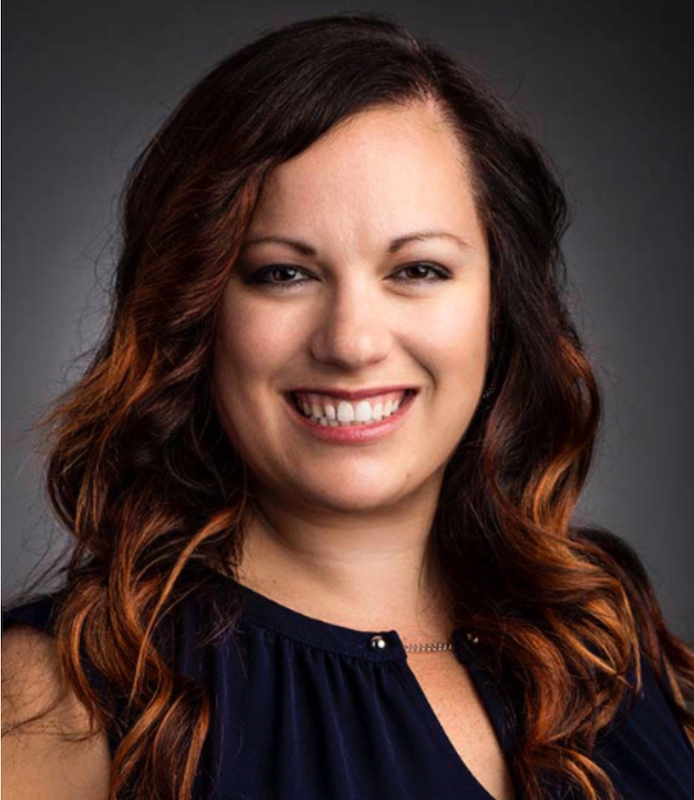 Jessica Ballard, standing in front of a gray back ground smiling forward