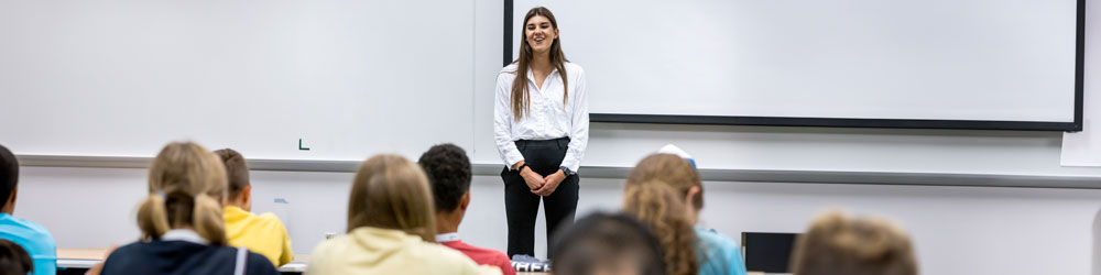 A woman standing in front of the classroom talking to other people in the seats
