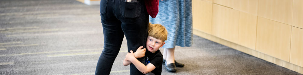 little boy clinging to an adults leg